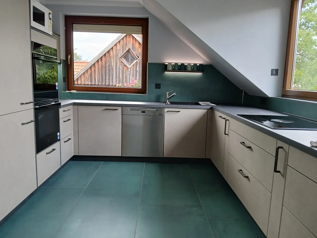 U-Küche in Betonoptik unter der Dachschräge mit grüner Wand