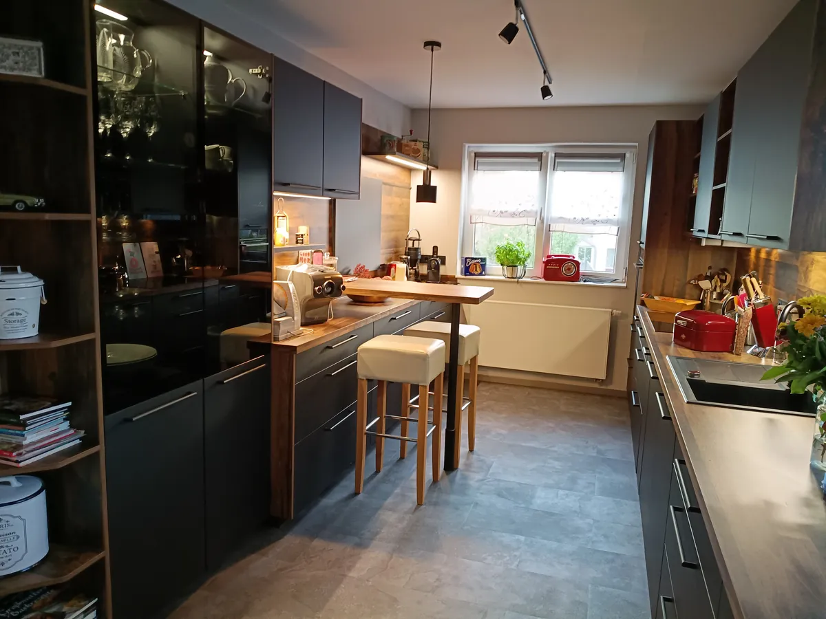 Schwarze Küche mit Holztheke, Barhockern und Glasvitrine